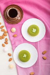 Obraz na płótnie Canvas Green mousse cake with pistachio cream and a cup of coffee on a white wooden background. top view, close up.