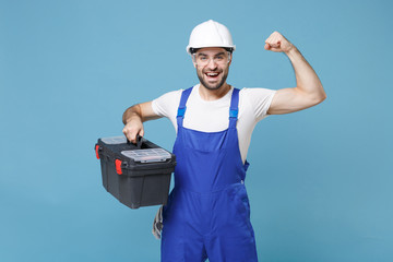 Strong man in coveralls helmet hardhat glasses hold tool case box isolated on blue wall background....