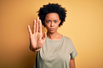 Young beautiful African American afro woman with curly hair wearing casual t-shirt doing stop sing with palm of the hand. Warning expression with negative and serious gesture on the face.