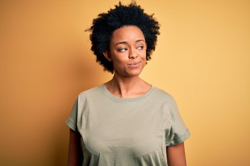 Obraz na płótnie Canvas Young beautiful African American afro woman with curly hair wearing casual t-shirt smiling looking to the side and staring away thinking.