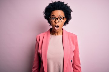 Fototapeta na wymiar Young beautiful African American afro businesswoman with curly hair wearing pink jacket afraid and shocked with surprise and amazed expression, fear and excited face.