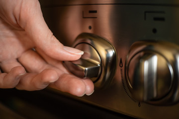 woman's hand turns on a switch on a stainless steel gas stove close up