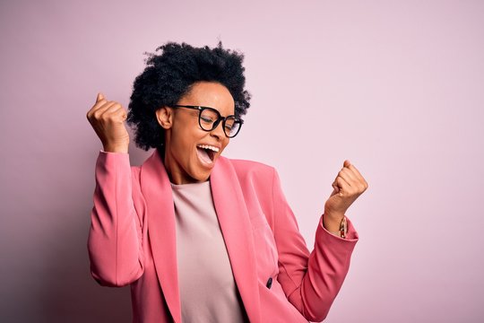 Young beautiful African American afro businesswoman with curly hair wearing pink jacket Dancing happy and cheerful, smiling moving casual and confident listening to music
