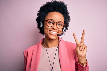 Young African American call center operator woman with curly hair using headset smiling with happy...