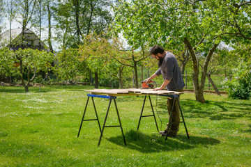 Mid adult caucasian man in the garden sanding wooden planks. DIY home improvement, restoration,...