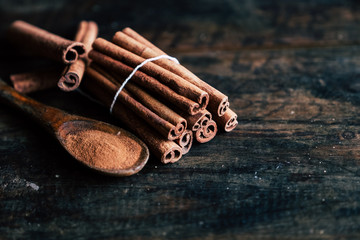 Batons de cannelle et cannelle moulue dans une cuillère en bois - Arrière plan sombre