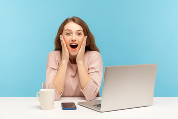 Wow, unbelievable! Surprised astonished young woman employee sitting at workplace with open mouth, shouting in amazement, shocked by unexpected news. indoor studio shot isolated on blue background