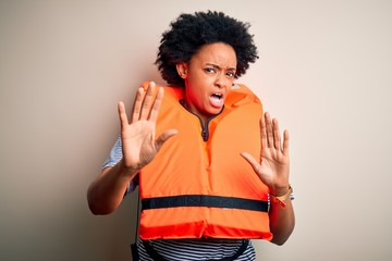 Young African American afro woman with curly hair wearing orange protection lifejacket disgusted...