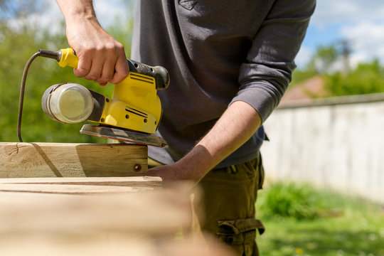Unrecognizable man in the garden sanding wooden planks. DIY home improvement, restoration, carpentry concept. Midsection hand detail shot.