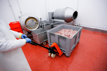 Frame image of a worker at a meat processing factory, pulls a load on which are crates of raw spicy meat. Process for the production of products of animal origin.