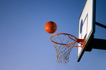 Street basketball ball falling into the hoop. Close up of orange ball above the hoop net with blue sky in the background. Concept of success, scoring points and winning. Copy space - Powered by Adobe