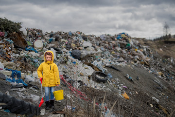 Front view of small child standing on landfill, environmental pollution concept.