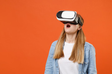 Shocked young woman girl in casual denim clothes posing isolated on bright orange wall background studio portrait. People sincere emotions lifestyle concept. Mock up copy space. Watching in headset.