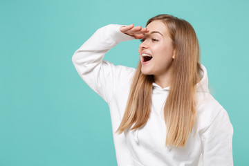Fototapeta premium Excited young woman girl in casual white hoodie posing isolated on blue turquoise background studio. People lifestyle concept. Mock up copy space. Holding hand at forehead looking far away distance.