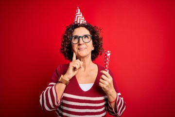 Middle age curly hair woman wearing birthday funny hat holding party trumpet on celebration serious face thinking about question, very confused idea