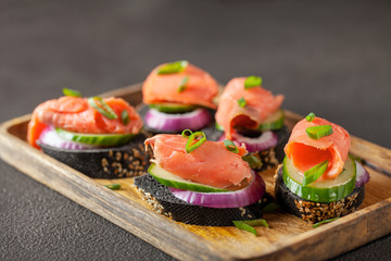 Smorrebrod, tapas or sandwich with onion, cucumber and salmon  on the cutting board.