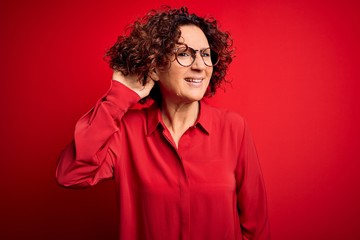 Fototapeta na wymiar Middle age beautiful curly hair woman wearing casual shirt and glasses over red background smiling with hand over ear listening an hearing to rumor or gossip. Deafness concept.