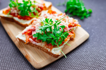 Fototapeta na wymiar Baked hot sandwiches on white bread with fried vegetables in tomato sauce, Servelat straws, melted cheese and green watercress on a wooden Board
