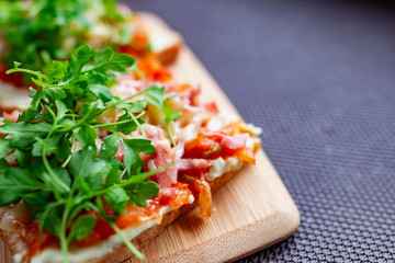 Baked hot sandwiches on white bread with fried vegetables in tomato sauce, Servelat straws, melted cheese and green watercress on a wooden Board