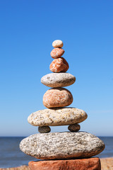 Fototapeta na wymiar Rock zen Pyramid of balanced stones against the background of the sea and blue sky.