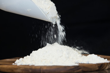  flour put on a wooden board and sprinkles from the scoop with a black background