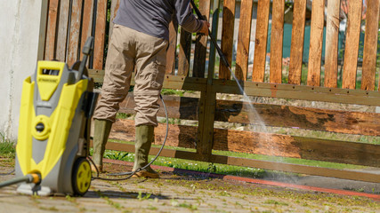 Unrecognizable man cleaning a wooden gate with a power washer. High water pressure cleaner  used to DIY repair garden gate.