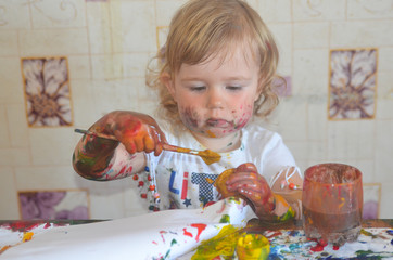 A preschool child toddler drawing with paints. The concept of stay at home. A little girl is home schooling during quarantine and coronavirus self isolation. Funny and humour kid