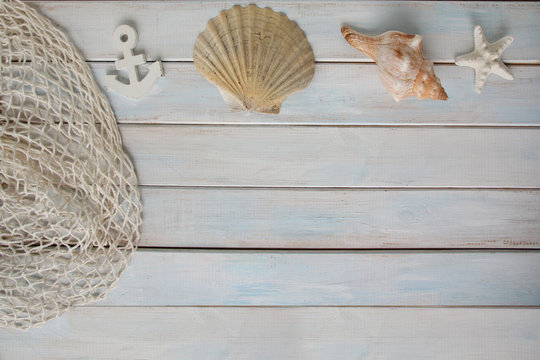 sea ​​shells, anchor, blue cord, white fishing net, starfish, pebbles on a white wooden background with place for text, concept of summer vacation, trip to warm lands, travel