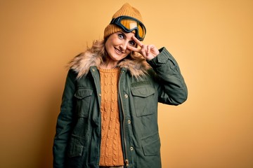 Middle age beautiful blonde skier woman wearing snow sportwear and ski goggles Doing peace symbol with fingers over face, smiling cheerful showing victory
