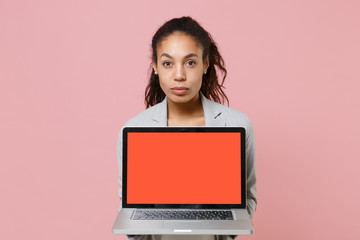 Beautiful young african american business woman in grey suit white shirt posing isolated on pink background. Achievement career wealth business concept Hold laptop pc computer with blank empty screen.