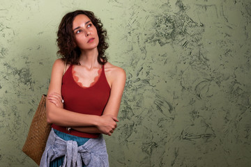 A curly-haired brunette stands in thought against a green wall