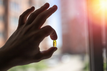 Holds vitamin D in a capsule with your fingers. Yellow vitamin d capsule in the fingers of a man's hand