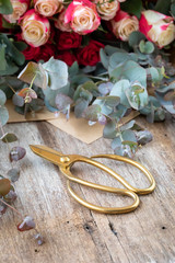 Gold florist scissors with rose and gum leaves background.