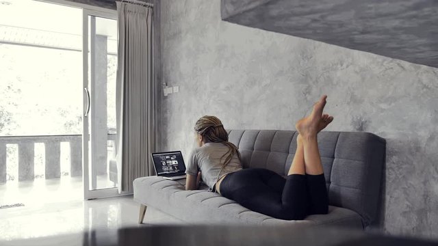 Woman on sofa reading news on a laptop in the open hall at home. Online Shopping, distance work or online education concept