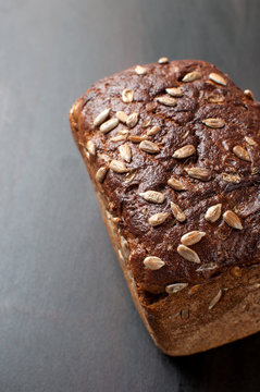 delicious fresh baked brown  bread with bran sunflower seeds on a dark background, vertical image
