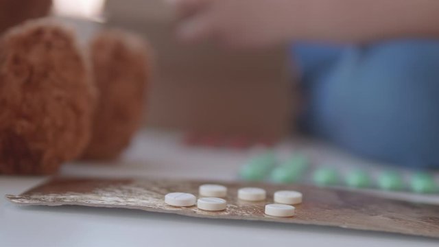 Kid plays with scattering medicine drugs. Toddler touches pills without parent control. Dangerous situation.