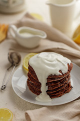 Stack of homemade chocolate pancakes topped with creamy yogurt sauce on a white plate. Delicious breakfast or dessert, rustic style, cozy food photography