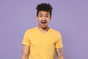 Fototapeta na wymiar Shocked perplexed young african american guy in casual yellow t-shirt posing isolated on pastel violet background studio portrait. People lifestyle concept. Mock up copy space. Keeping mouth open.