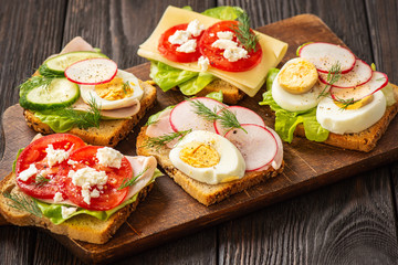 Toasts with eggs, cheese, ham, radish, cucumbers and tomatoes , breakfast idea.