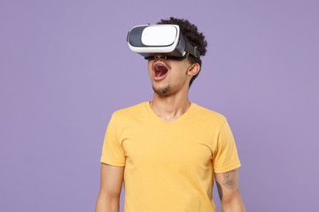 Shocked young african american guy in casual yellow t-shirt posing isolated on pastel violet background studio. People lifestyle concept. Mock up copy space. Watching in headset, keeping mouth open.