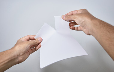 hands breaking a sheet of paper on white background