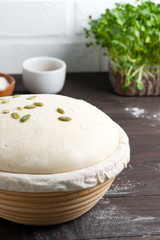 Homemade freshly prepared yeast dough in a basket for baking with pampkin seeds on a dark wooden background.