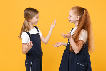 Two young little girls 12-13 years old in white t-shirt blue school uniform dresses isolated on yellow background children studio portrait Childhood kids education lifestyle concept Mock up copy space