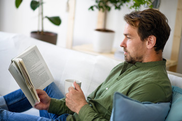 Man sitting on sofa and reading book at home, lockdown concept.