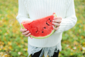 A piece of watermelon in the hands of a girl on an autumn day.