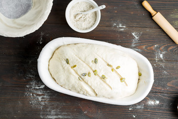 Top view of homemade freshly cooked raw loaf with pumpkin seed in a basket on a wooden dark background.