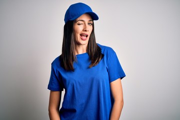 Young delivery woman with blue eyes wearing cap standing over blue background winking looking at the camera with sexy expression, cheerful and happy face.