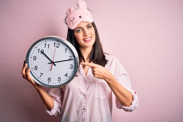 Young brunette woman with blue eyes wearing pajama holding big clock at night time very happy...