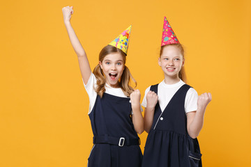 Two birthday girls 12-13 years old in white t-shirt blue school uniform dresses hat isolated on yellow background children studio portrait Childhood kids education lifestyle concept Mock up copy space