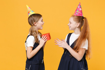 Two birthday girls 12-13 years old in white t-shirt blue school uniform dresses hat isolated on yellow background children studio portrait Childhood kids education lifestyle concept Mock up copy space